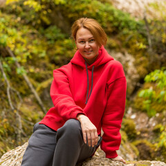 Naklejka na ściany i meble a girl in a red hoodie is sitting on a rock on the edge of the forest.