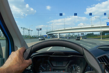 The driver's hand on the steering wheel of a car. View of the road through the steering wheel of the car.
