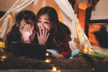 Happy asian mother tells stories to her daughters with digital tablet in magic night. Family merry christmas and new year holiday concept.