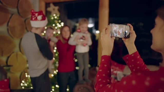 Bokeh - Woman taking photos of a young family of four with her smartphone in front of a Christmas tree in a beautiful cottage