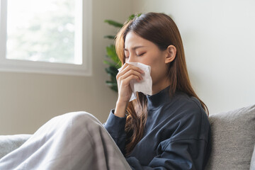 Sick at home concept. Woman sneezing on the sofa in winter season.