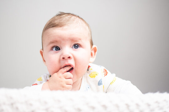 baby lying on stomach with finger in mouth, questioning look