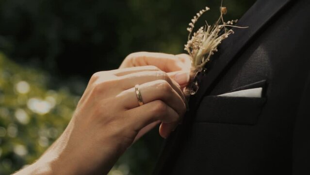 Groom puts on a boutonniere. A girl, a bride or bridesmaid, straightens a flower buttonhole on a man's suit. bow tie bride . slow motion