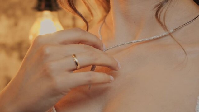 The bride hand straightens the necklace. Bride dresses a necklace. The girl hand straightens the necklace. A young woman puts on a chain with a pendant around her neck. Girl dresses a necklace.
