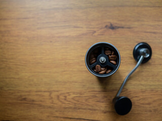 Coffee hand grinder steel and bean coffee inside show top view ready to grind, on table wood backgroud..