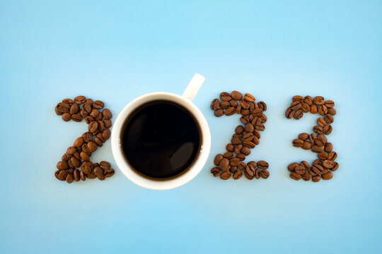 2023 number made of coffee beans and cup of coffee on light blue background as symbol of new start, goals and beginning. Happy New Year and Merry Christmas postcard or greeting card.
