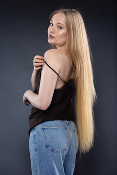 Young blonde woman in jeans and brown singlet on gray background