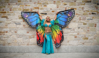 professional belly dancer posing with colorful butterfly wings and authentic dress in front of wall