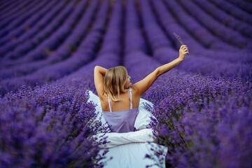 A middle-aged woman sits in a lavender field and enjoys aromatherapy. Aromatherapy concept, lavender oil, photo session in lavender