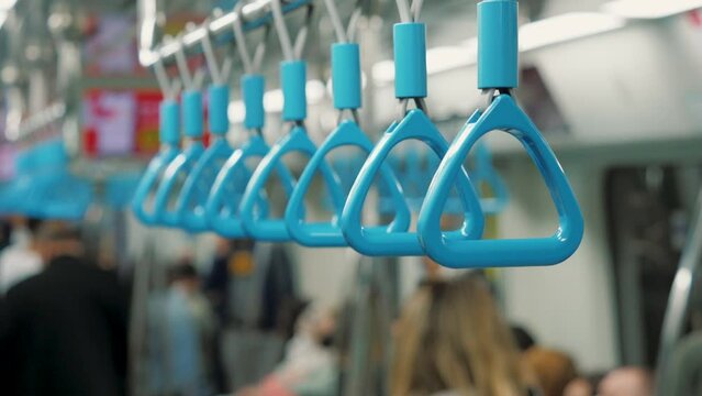 Hanging alley of public transportation, metro train interior. Close up of handles hanging on moving train, passengers inside, blurred background