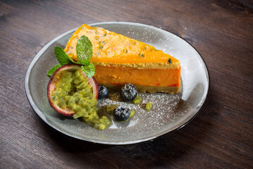 Passion fruit cheesecake. A delicate dessert portion with fresh passionfruit wedges and blueberries on a plate.