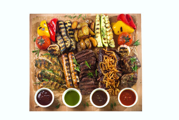 A board with grilled appetizers and sauces. Grilled vegetables and meat snacks: sausages, chicken fillets, pork and beef steaks.