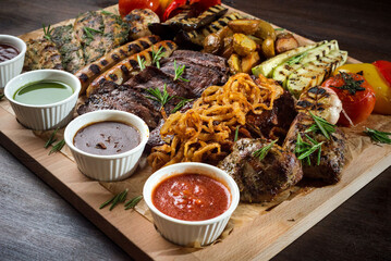 A board with grilled appetizers and sauces. Grilled vegetables and meat snacks: sausages, chicken fillets, pork and beef steaks.