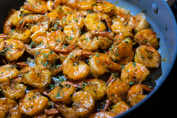 Closeup image of jumbo shrimp being sauteed in a pan with oregano, chive, rosemary, garlic and...