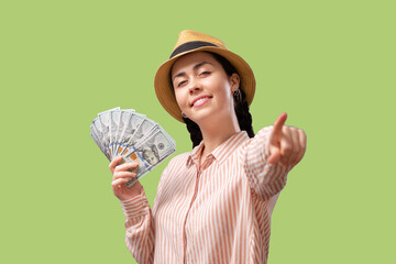 Winning the lottery. A young Caucasian happy woman hold a fan of dollars and point index finger. Light green background. The concept of stock market trading and investment