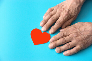hands of an old man heart red paper-cut on a blue background. Love for elderly parents concept. caring for the elderly. Retired heart health