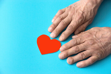 Fototapeta premium hands of an old man heart red paper-cut on a blue background. Love for elderly parents concept. caring for the elderly. Retired heart health