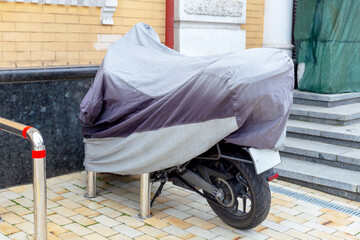 Fototapeta na wymiar A motorcycle on the street is covered with a cover