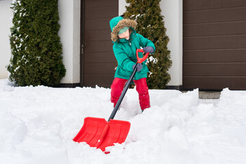 Child playing in  snow with shovel. Girl shoveling fresh snow and clearing sidewalks near home...