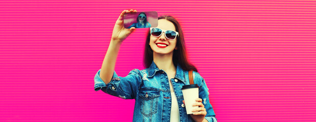 Portrait of happy smiling young woman taking selfie with smartphone wearing backpack on pink background