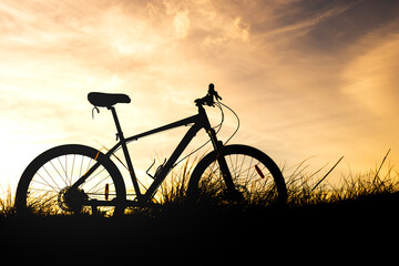 Fototapeta na wymiar silhouette of a bicycle in the grass against an orange sky during sunset