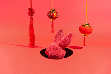 A red rabbit in a hole surrounded by New Year's decorations on a red background. Chinese rabbit New...