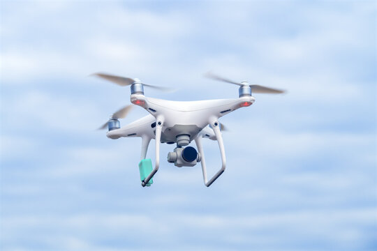 White drone with camera in flight against blue cloudy sky