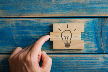 Male finger pushing a wooden peg into a stack of them to complete a light bulb shape drawn on them