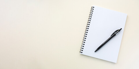 Notebook on a spiral on a plain beige background. Blank white sheets in a note. Flat lay, banner, top view, copy space