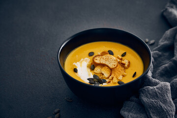 Pumpkin cream soup with croutons on dark background