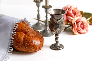 Challah bread covered with a special napkin, shabbat wine and candles on white bacground....