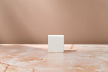 White squared podium, pedestal on beige pink marble background and shadows on the wall. Blank, scene. Mockup. Mock up.