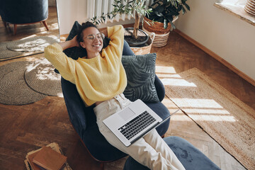 Top view of happy young woman using laptop while sitting in a comfortable chair at home