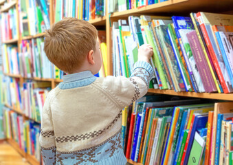 A little boy in a public library chooses a book for himself. The kid is drawn to knowledge. The kid takes a book from the shelf.