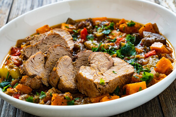 Roast pork loin with sweet potatoes and mix of cooked vegetables served on wooden table

