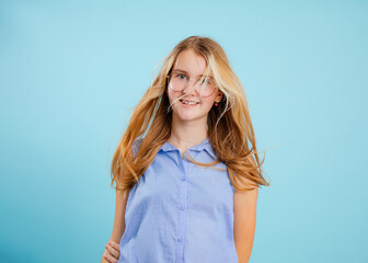 Smiling, positive teen blond girl in glasses in blue shirt with trendy hairstyle on blue isolated...