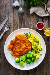 Breaded fried pork chop with boiled potatoes and brussels sprouts  on wooden table
