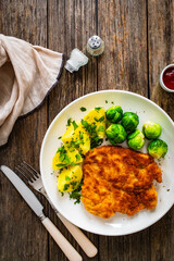 Breaded fried pork chop with boiled potatoes and brussels sprouts  on wooden table
