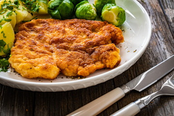Breaded fried pork chop with boiled potatoes and brussels sprouts  on wooden table
