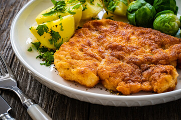 Breaded fried pork chop with boiled potatoes and brussels sprouts  on wooden table
