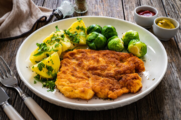 Breaded fried pork chop with boiled potatoes and brussels sprouts  on wooden table
