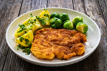 Breaded fried pork chop with boiled potatoes and brussels sprouts  on wooden table
