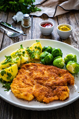 Breaded fried pork chop with boiled potatoes and brussels sprouts  on wooden table
