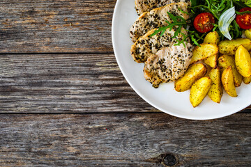 Fried pork loin with baked potatoes and fresh green  vegetables on wooden table
