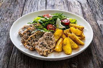 Fried pork loin with baked potatoes and fresh green  vegetables on wooden table
