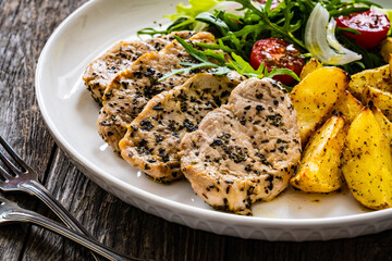 Fried pork loin with baked potatoes and fresh green  vegetables on wooden table
