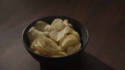 organic potato chips with black pepper in black bowl on walnut table