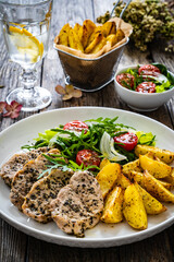 Fried pork loin with baked potatoes and fresh green  vegetables on wooden table
