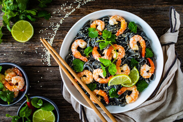 Black rice noodles with fried prawns and coriander on wooden table
