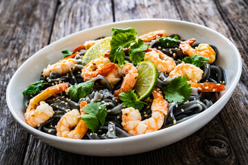 Black rice noodles with fried prawns and coriander on wooden table
